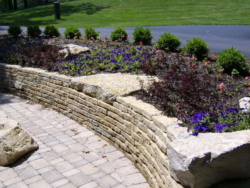 Curved dry-laid stone wall holding a planted bed above a paver walk, with large capstones